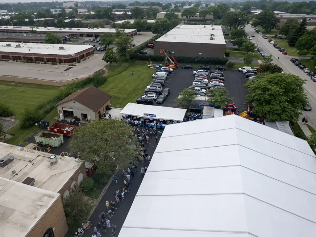Overhead view showing a long line of attendees waiting near a smaller tent used for food distribution at Greek Fest.