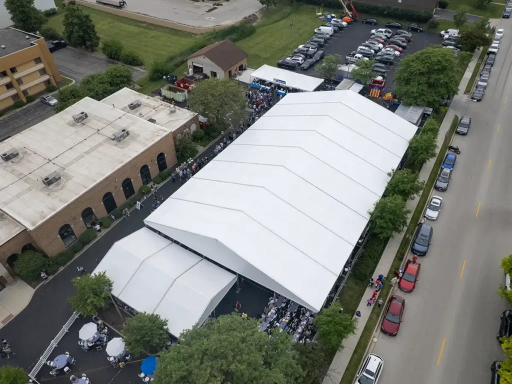 Wide aerial view of Greek Fest tents set up in a church lot with attendees filling the space beneath them.
