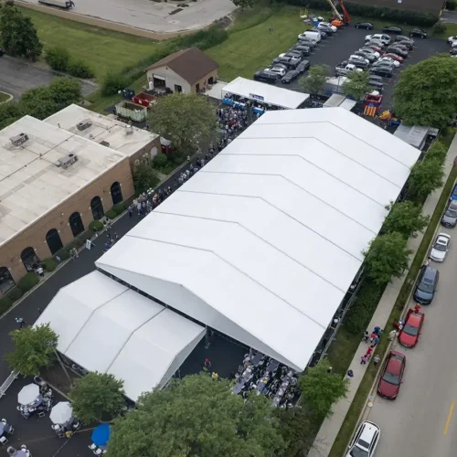 Wide aerial view of Greek Fest tents set up in a church lot with attendees filling the space beneath them.