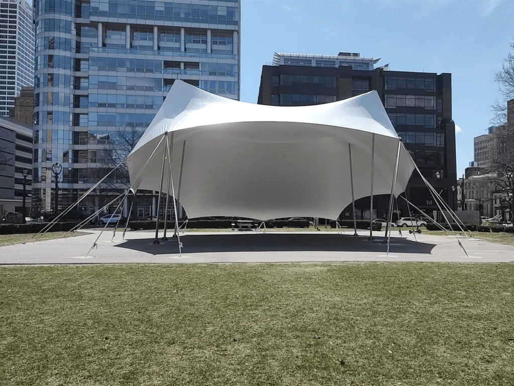White bandshell-style tension tent set up in a circular paved area surrounded by office buildings