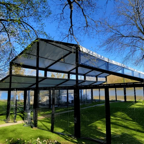 Black-framed clearspan tent with transparent sidewalls overlooking a lake