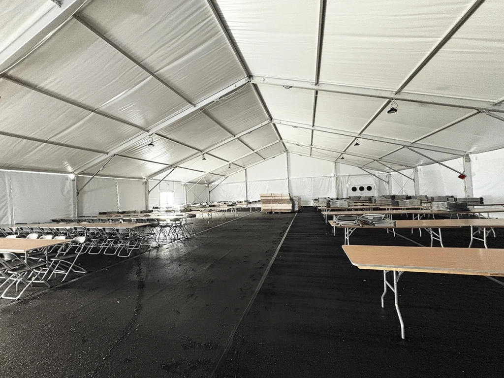 Interior of a white frame tent set up with folding tables and chairs arranged in rows for dining or break service.
