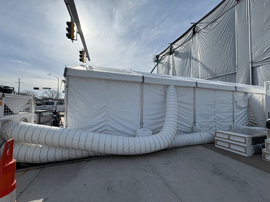 Exterior of a white tent with HVAC ducting tubes and cooling equipment.