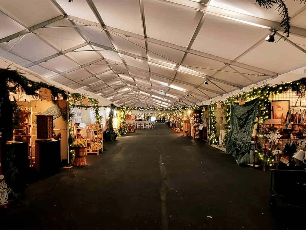Interior view of a decorated clearspan tent set up as a holiday vendor market with string lights