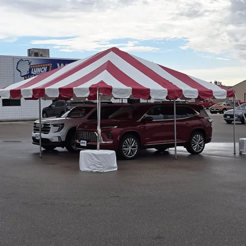 Red and white striped pole tent installed over parked vehicles in a dealership lot