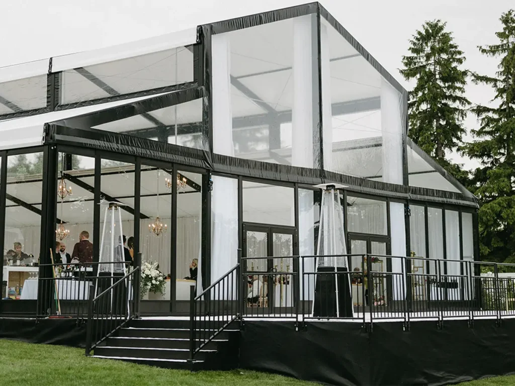 Modern black-frame LEVO clear structure with glass walls and chandeliers, installed by JK Rentals for a wedding reception.