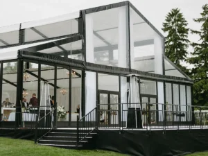 Modern black-frame LEVO clear structure with glass walls and chandeliers, installed by JK Rentals for a wedding reception.