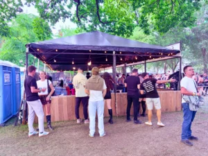 Open bar tent with black roof, string lights, and a wooden bar front serving guests at ARC Music Festival.