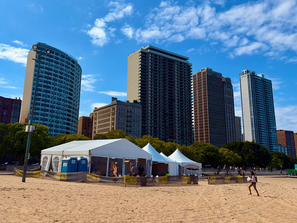 White frame tents and portable restrooms set up along the beach with Chicago high-rises in the background.