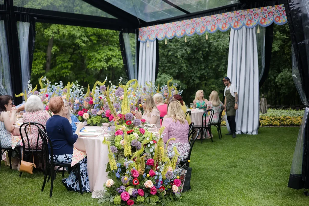 Guests seated inside a clearspan tent with large, colorful floral arrangements lining the tables.