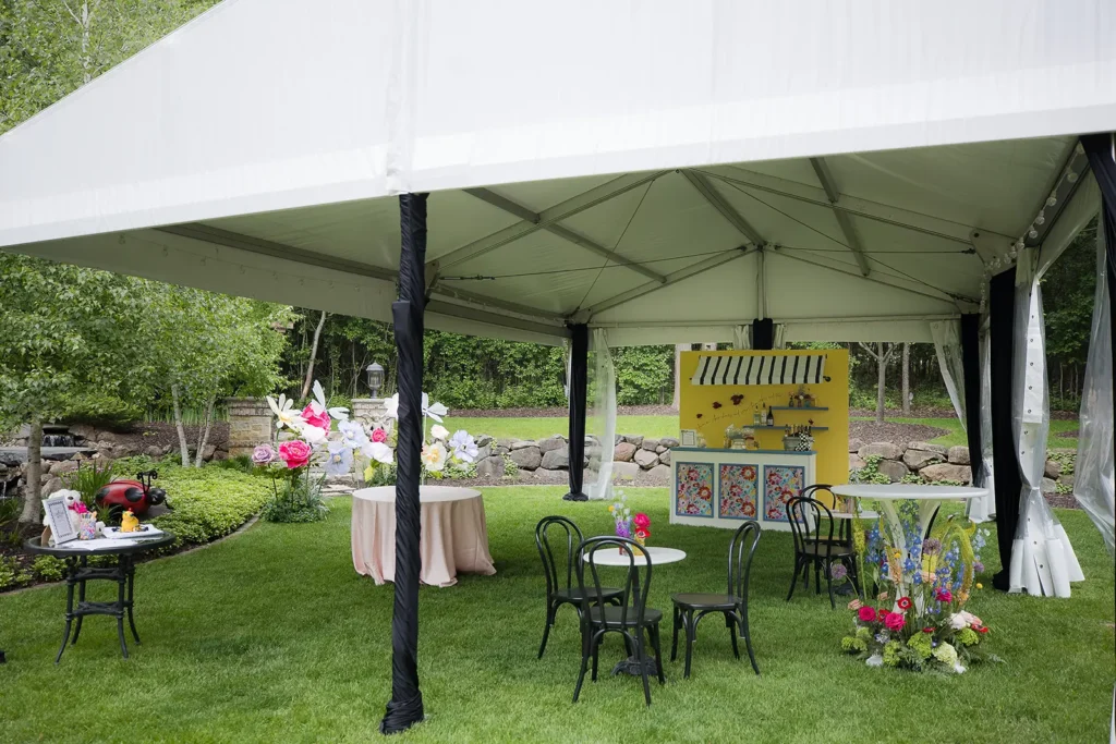 Wide view of the lounge tent showing the yellow bar backdrop, round tables, floral accents, and surrounding garden landscape.
