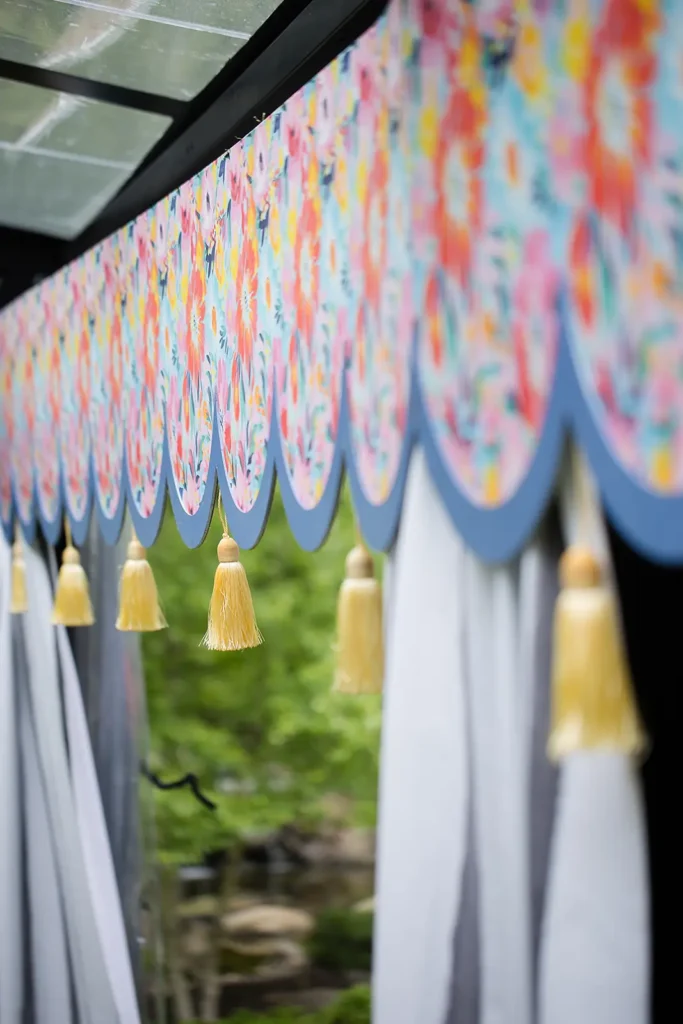 Close-up of a colorful scalloped valance with hanging tassels inside a clearspan tent at a garden baby shower.