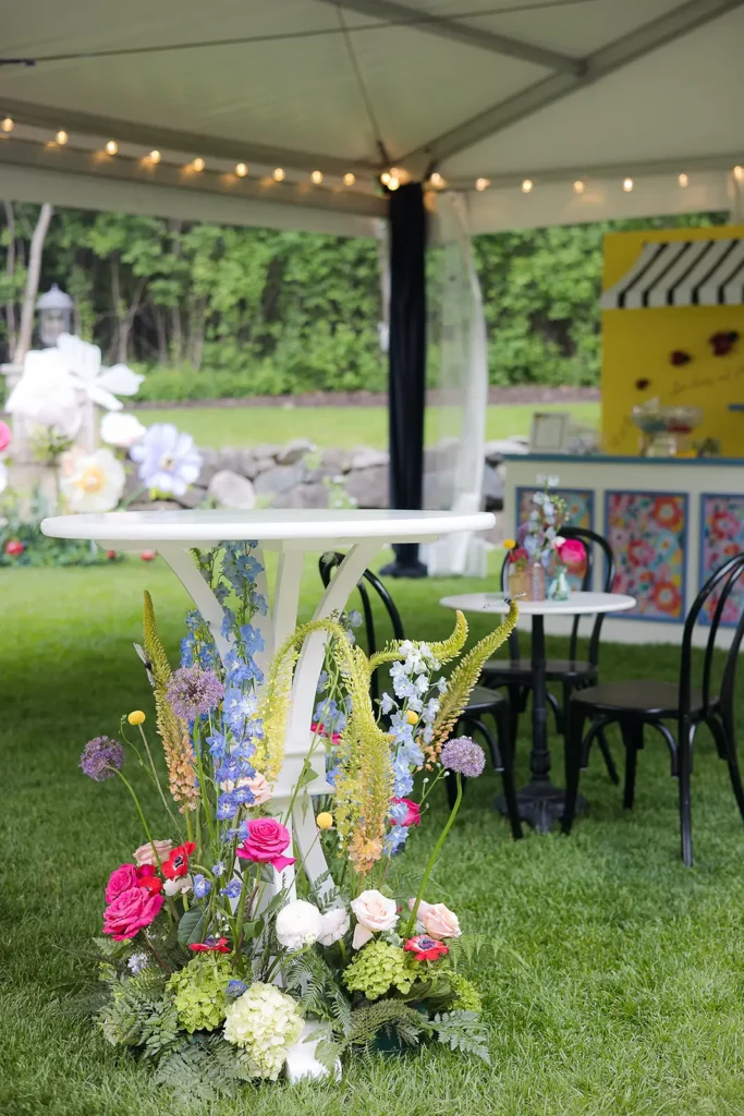 White high-top table surrounded by lush pastel florals under a tented cocktail area on the lawn.
