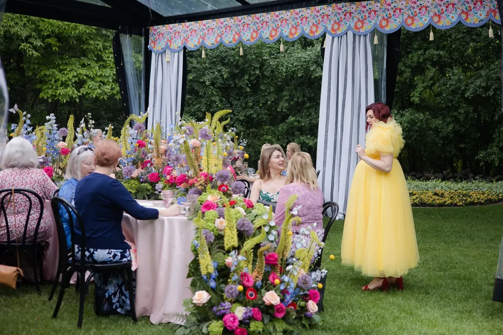 Mom-to-be in a bright yellow dress smiles while standing beside floral décor inside a clearspan tent.