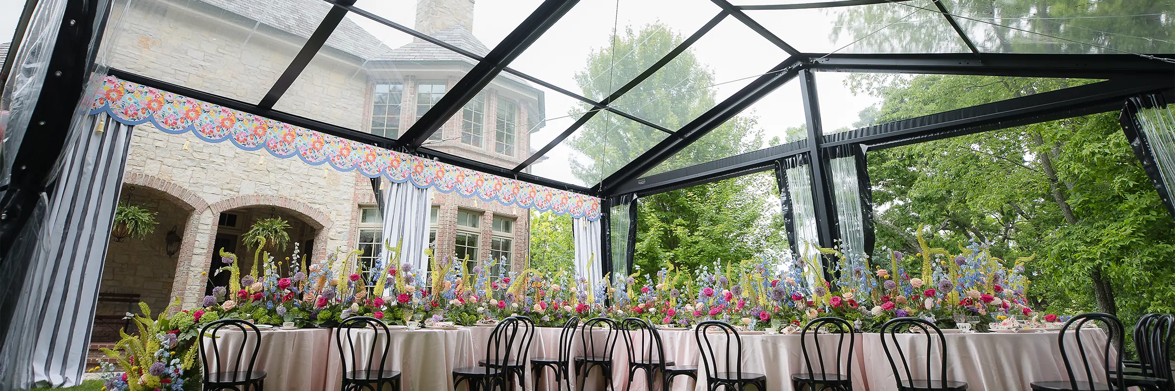 Overhead view of round tables arranged in a U-shape with colorful floral arrangements under a clear tent.