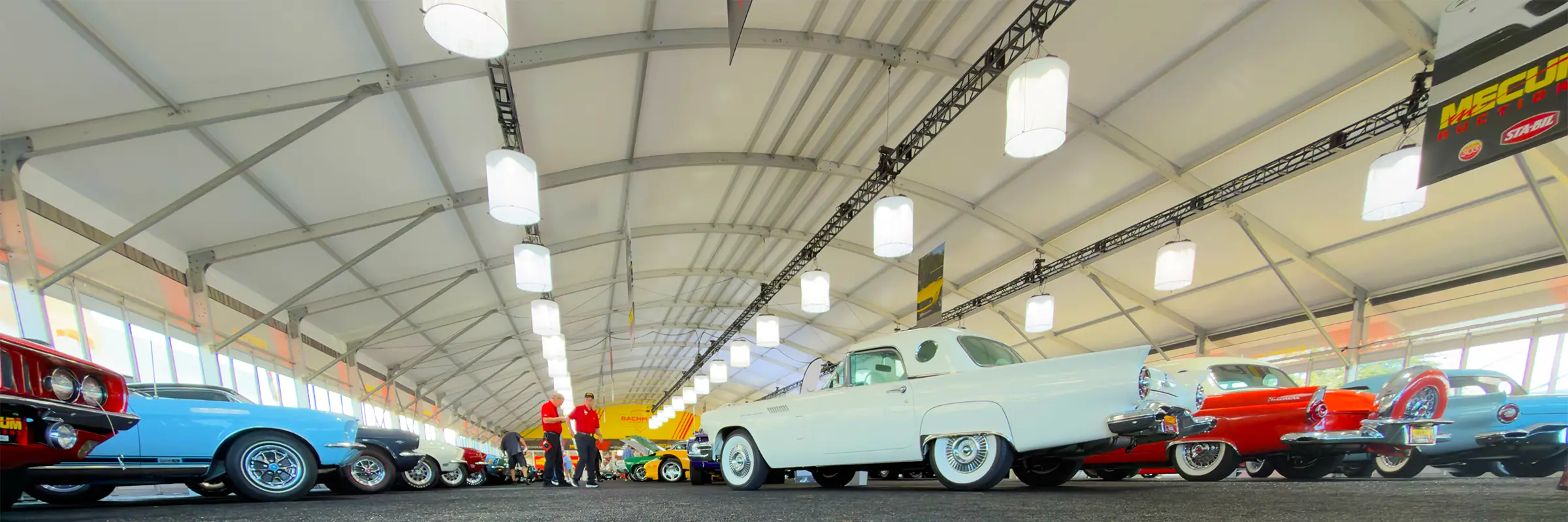 Low-angle view of classic cars lined up inside a JK Rentals arcum clearspan at Mecum Auto Auctions in Kissimmee, FL.