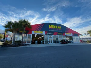 Front elevation of a JK Rentals clearspan with glass entry doors and Mecum Auctions branding, set among palm trees in Kissimmee, Florida.