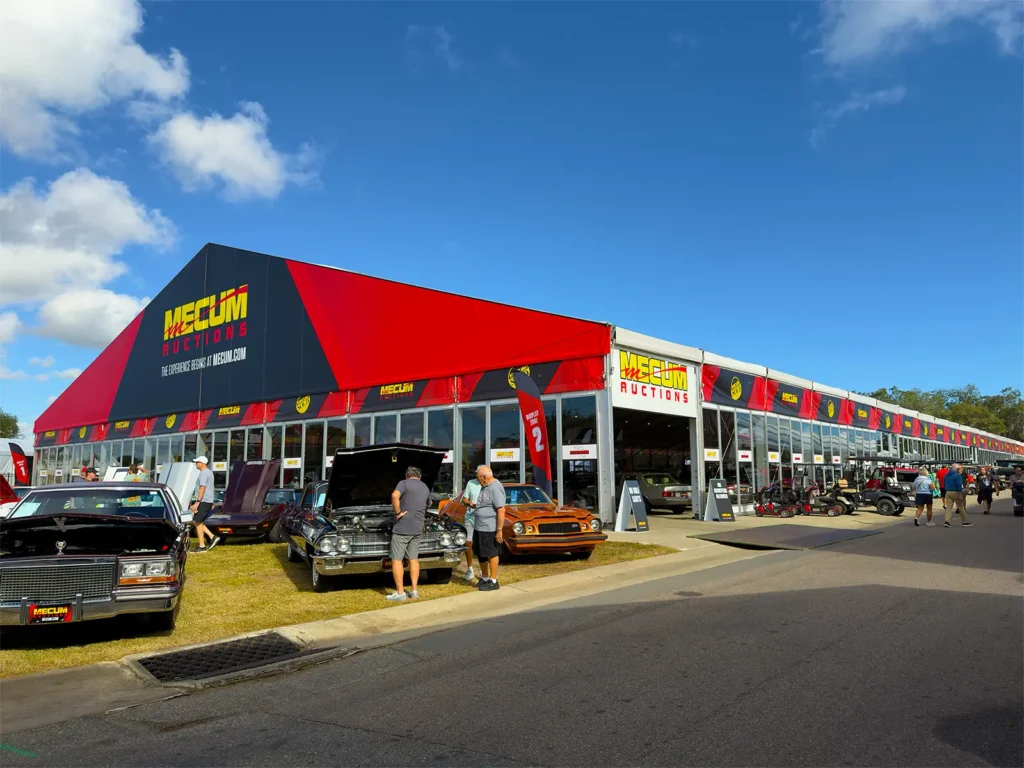 Exterior view of a JK Rentals clearspan structure with glass walls and Mecum Auctions branding, with classic cars displayed outside in Kissimmee, Florida.