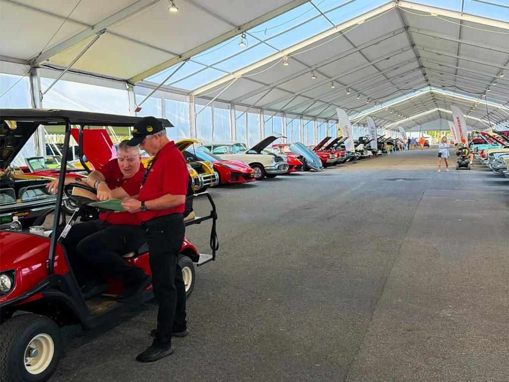 Long aisle inside a frame tent with clear vinyl sidewalls, featuring staff and vehicle displays at Mecum Auto Auctions in Kissimmee, Florida.