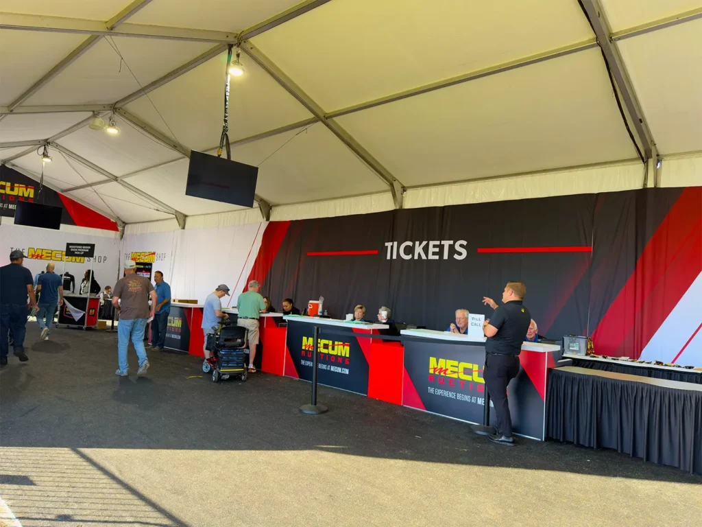 Ticket counters and check-in area inside a JK Rentals frame tent with branded graphics at Mecum Auto Auctions, Kissimmee, FL.