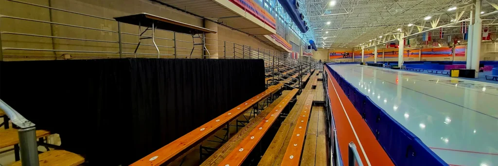 Temporary pipe and drape barrier installed alongside bleacher seating inside an indoor ice rink venue.