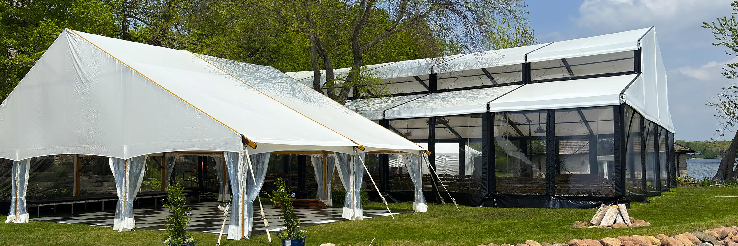 Exterior view of a 20m x 25m Levo clearspan structure by the lake with an adjacent white frame tent during a wedding setup in Oconomowoc, Wisconsin.