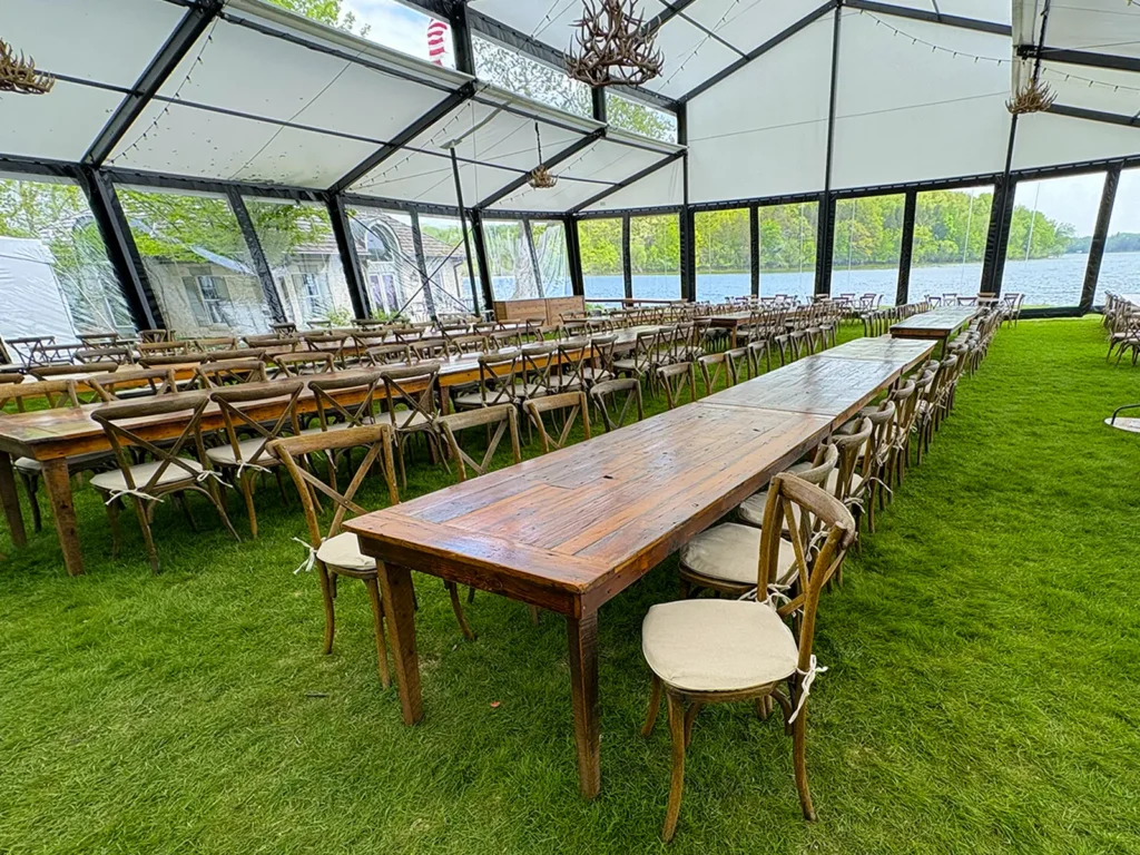 Reception tables arranged inside a Levo clearspan structure with clear wall panels and lake views during a wedding setup in Oconomowoc, Wisconsin.