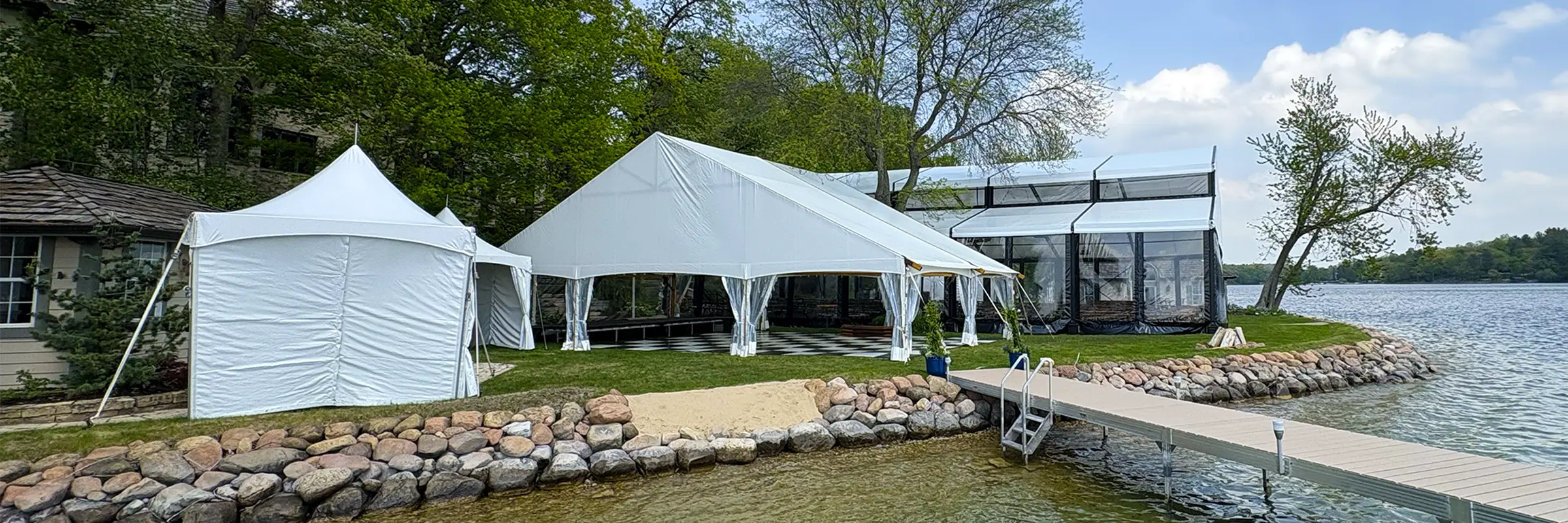 Wide shoreline view of the waterfront wedding tent layout with a Levo clearspan structure and support tents in Oconomowoc, Wisconsin.