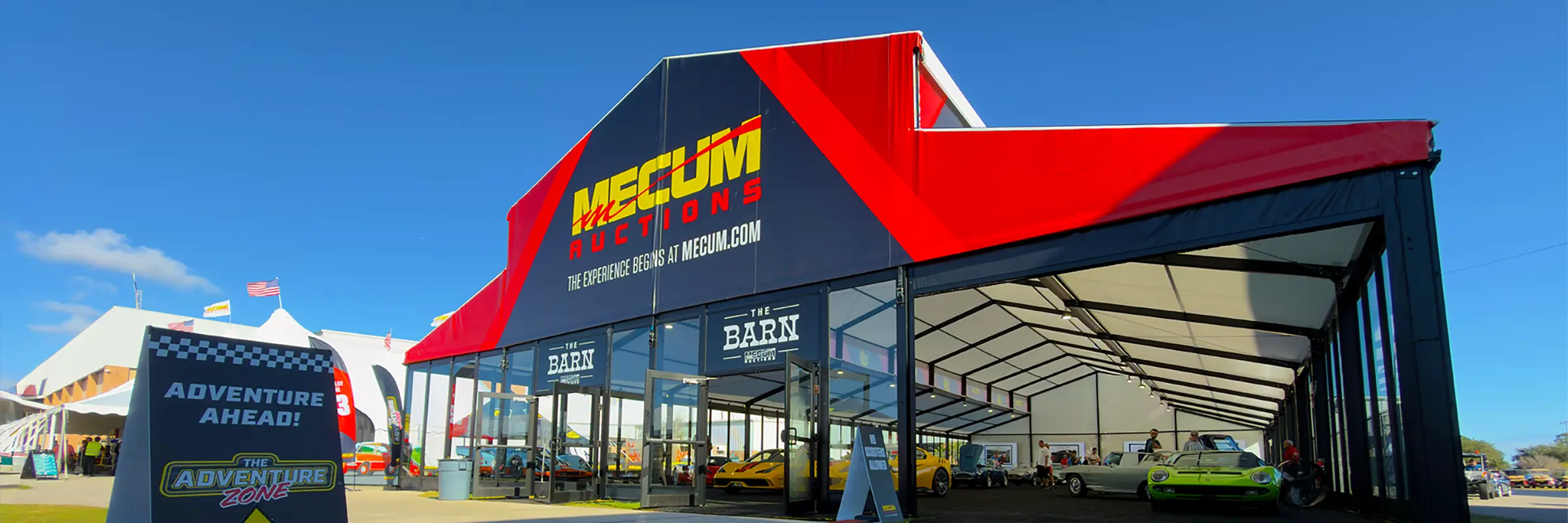 Mecum Auctions “The Barn” branded clearspan structure with a glass front entrance and classic cars inside.