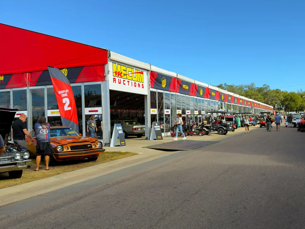 Long glass-wall clearspan structure at Mecum Auto Auctions in Kissimmee, Florida with display zone signage and classic cars outside.