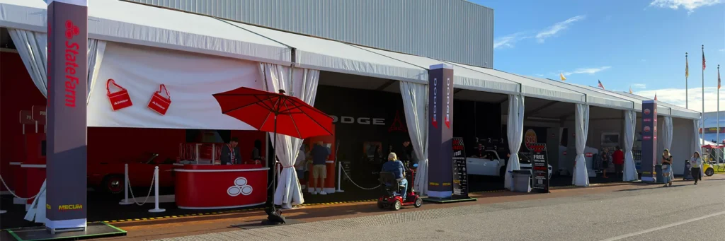Outdoor row of sponsor and vendor booths under a long white event tent at Mecum Auto Auctions in Kissimmee, Florida.