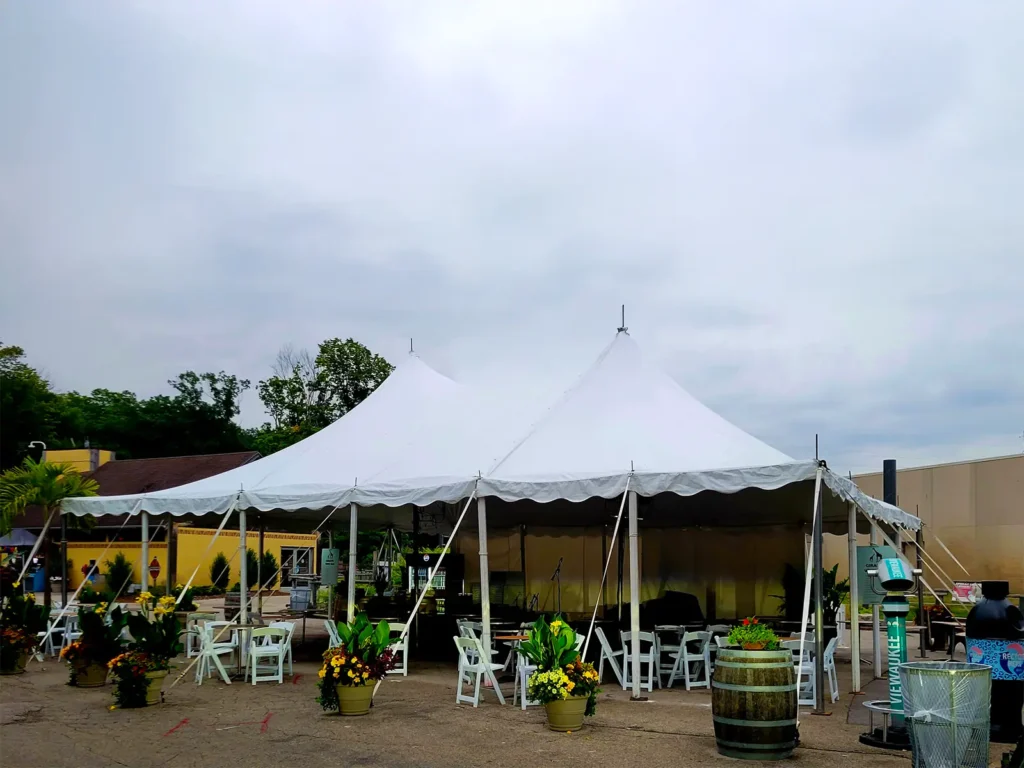 Large white high-peak pole tent set as a seating zone with cafe tables, chairs, and floral planters during Zoo A La Carte at Milwaukee County Zoo.