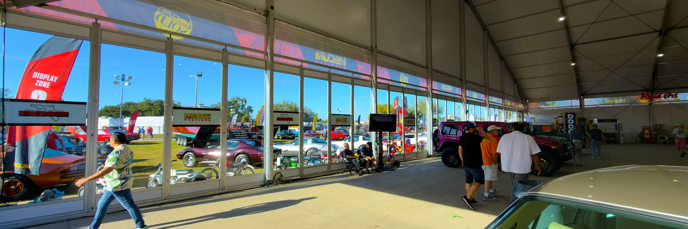 Inside a JK Rentals clearspan with glass walls at Mecum Auto Auctions in Kissimmee, Florida, looking out to display vehicles and signage.