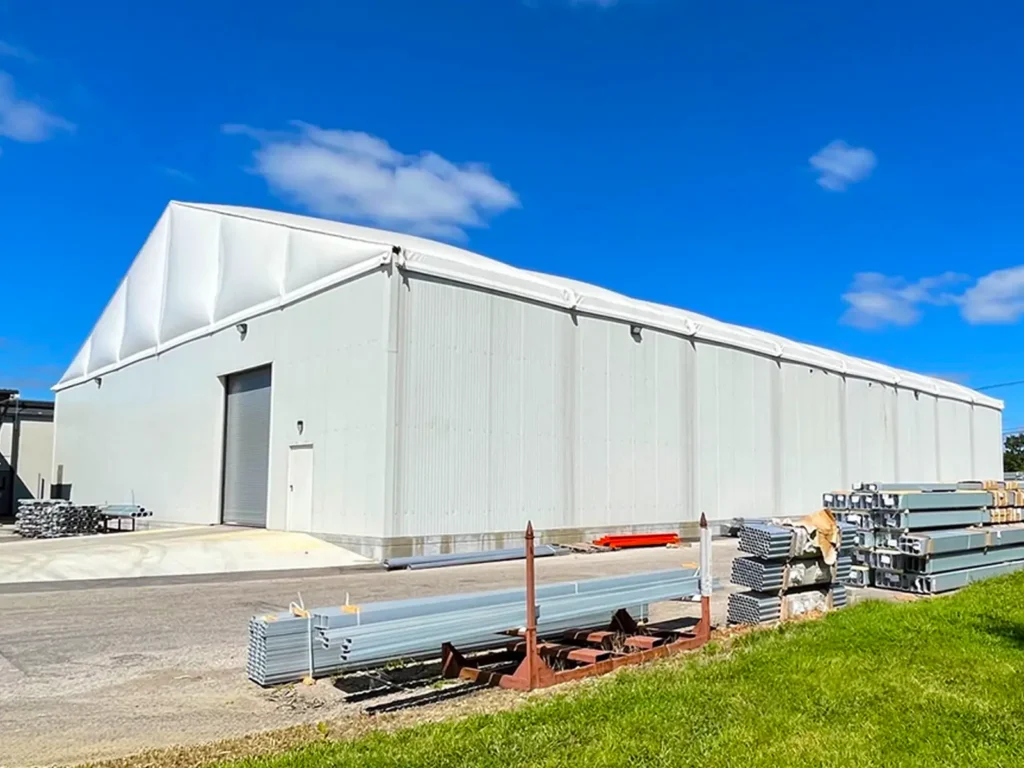 Angled view of a long hard-wall clearspan warehouse showing the full sidewall run and worksite materials in the foreground.