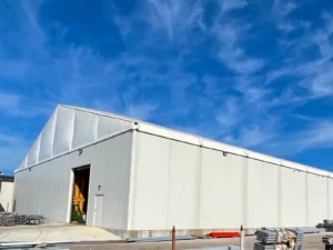 Hard-wall clearspan warehouse exterior with roll-up door partially open, showing equipment inside near the entry.