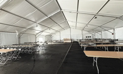 Interior of a white frame tent set up with folding tables and chairs arranged in rows for dining or break service.